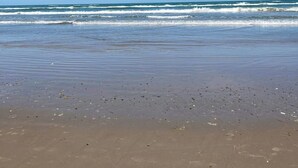 Ein Strand mit Wellen, blauem Himmel und sandigem Ufer.