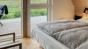 Ein Schlafzimmer mit einem großen Bett, einem Sessel und Blick durch eine Glastür auf eine Terrassenanlage.
