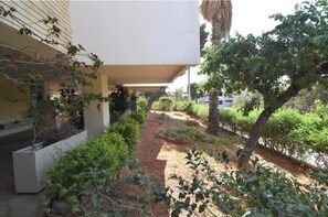A courtyard with a pathway, a white building, and various plants. - Vouliagmeni Lake Central Apartment (Vouliagmeni)