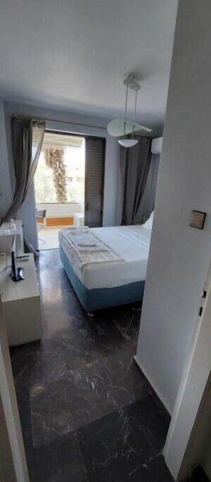 A bedroom with a bed, a bedside table, a ceiling fan, and a window with curtains. - Vouliagmeni Lake Central Apartment (Vouliagmeni)