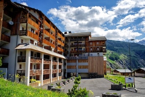 Um hotel com vários andares, varandas, área de estacionamento e montanhas ao fundo.