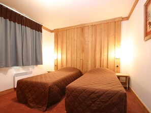 Une chambre avec deux lits, des murs recouverts de panneaux de bois, une fenêtre avec des rideaux et des lampes fixées au mur.