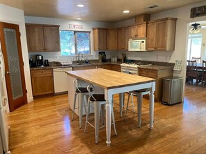 A kitchen with wooden cabinets, a central island with stools, a refrigerator, and a window with a view.