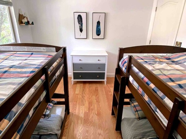 A room with two wooden beds, a white dresser, and two framed feathers on the wall.