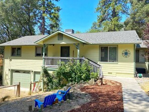 A two-story house with a front porch, a garage, and a yard with mulch and a blue chair. - Mountain Family Cottage Ideal for Outdoor Adventures in Ohio (Wishon)