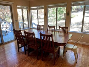A dining room with a large wooden table and six chairs, large windows with blinds, and a view of a deck and outdoor area. - Mountain Family Cottage Ideal for Outdoor Adventures in Ohio (Wishon)