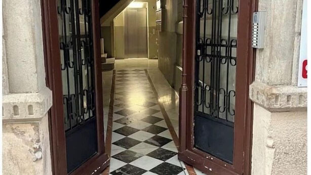 Um corredor com piso xadrez que leva a uma escadaria.
