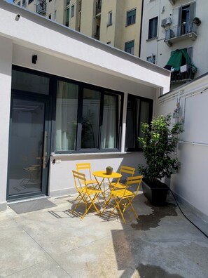 A small outdoor patio with a table and chairs, a potted plant, and a building with multiple windows and balconies in the background. - Spacious apartment in Navigli area with parking (Milano)