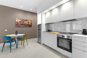 Een moderne keuken met witte kasten, een inbouwoven en een eethoek met een ronde tafel en kleurrijke stoelen.