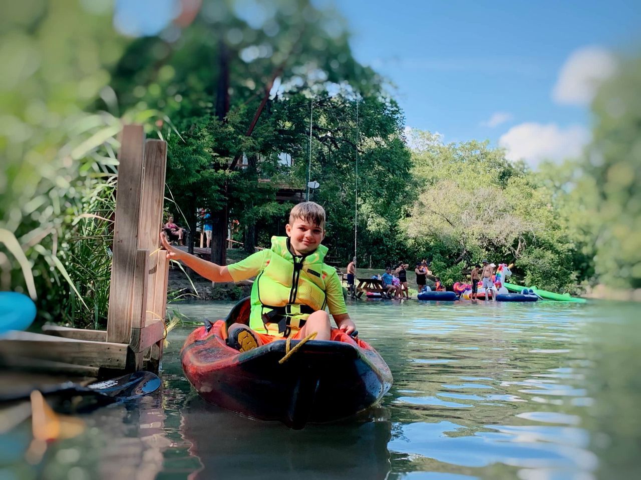 Une personne dans un kayak sur une voie navigable, avec d’autres kayaks et des personnes en arrière-plan.