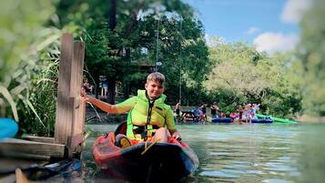 Une personne dans un kayak sur une voie navigable, avec d’autres kayaks et des personnes en arrière-plan.