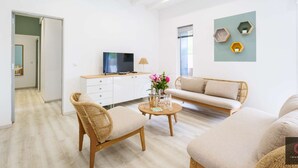 Ein modernes Wohnzimmer mit einer Couch, zwei Sesseln, einem Couchtisch, einem Fernseher und dekorativen Wandregalen.