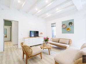 Ein modernes Wohnzimmer mit einer Couch, zwei Sesseln, einem Couchtisch, einem Fernseher und dekorativen Wandregalen.