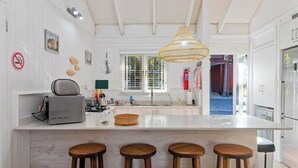 A kitchen with a central island, bar stools, a hanging light fixture, a fire extinguisher, and a window with blinds.