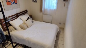 Un dormitorio con cama, ventana con cortinas, radiador y un adorno en la pared.