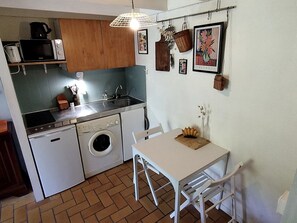 Eine kleine Küche mit Waschmaschine, Mikrowelle und Spüle. Ein Esstisch mit Stühlen und eine Hängelampe sind vorhanden.