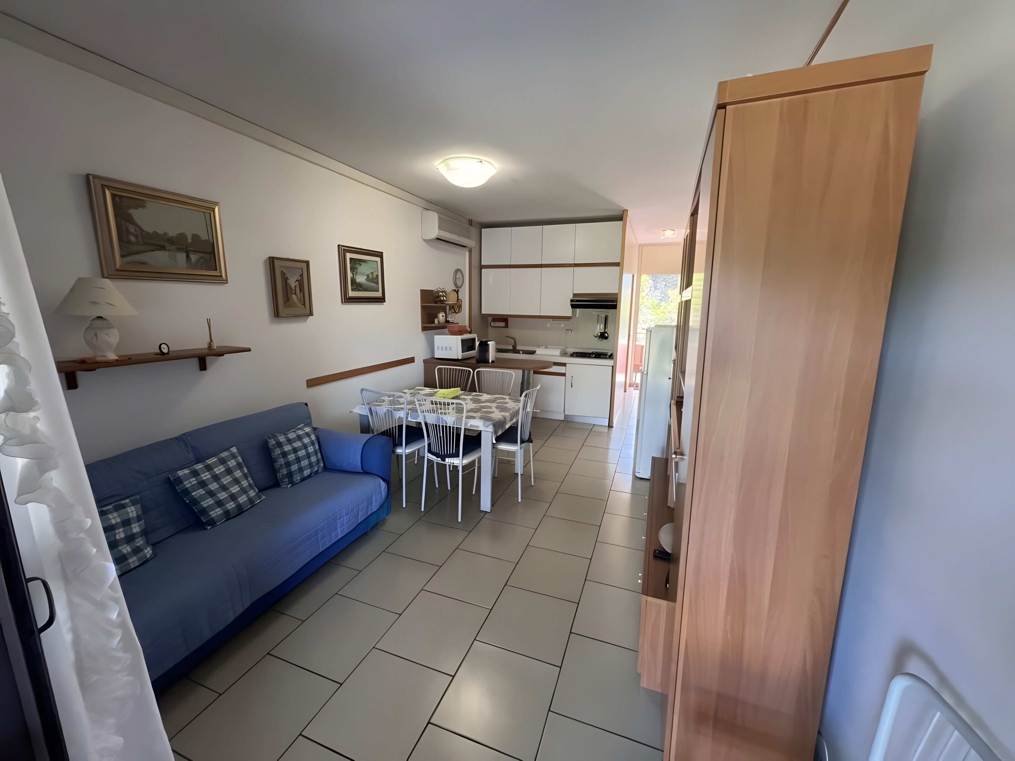 Un espacio habitable compacto con sofá, mesa de comedor, zona de cocina y un armario de madera.