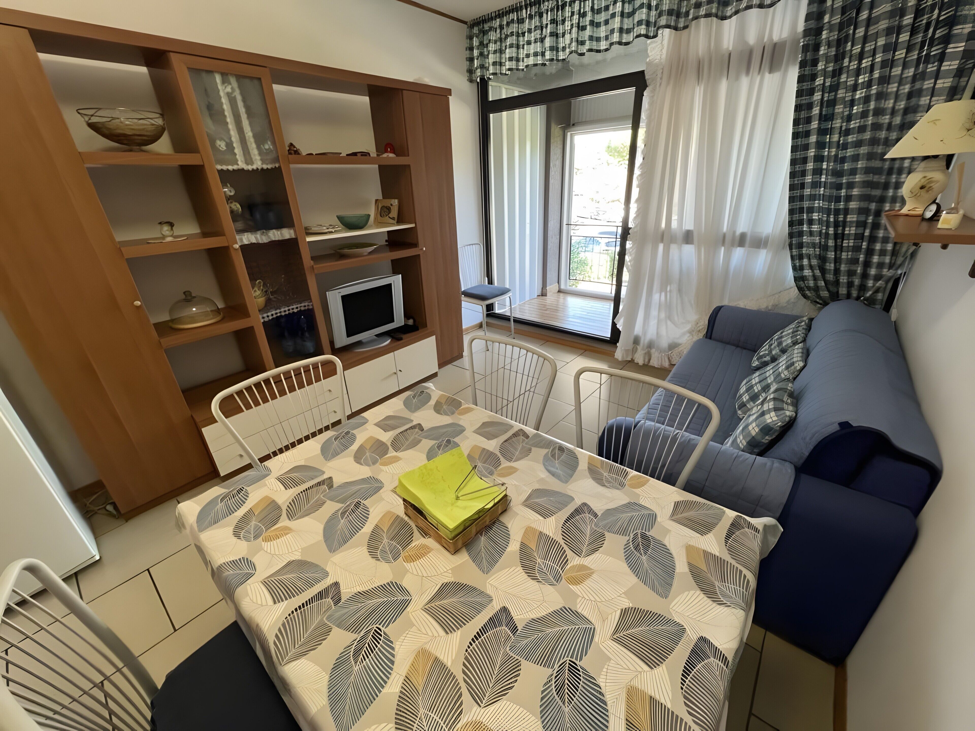 Un salon comprenant un canapé, une table à manger avec des chaises, un téléviseur et un meuble en bois avec des étagères.