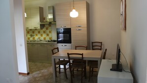 A modern kitchen with a dining table and chairs, a built-in oven, and a hanging light fixture. - Apartment 'Bilocale con Giardino Privato' with Exclusive Garden (Marina di Bibbona)