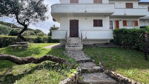 A two-story building with a stone staircase leading to the entrance, surrounded by greenery and a tree. - Apartment 'Bilocale con Giardino Privato' with Exclusive Garden (Marina di Bibbona)
