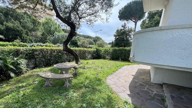 A garden with a stone table and chairs, a hedge, and a building with a white exterior. - Apartment 'Bilocale con Giardino Privato' with Exclusive Garden (Marina di Bibbona)