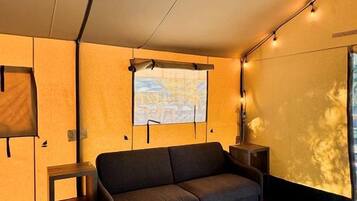 Une pièce confortable avec un canapé, une petite table, une fenêtre donnant sur un beau paysage et un projecteur fixé au mur.