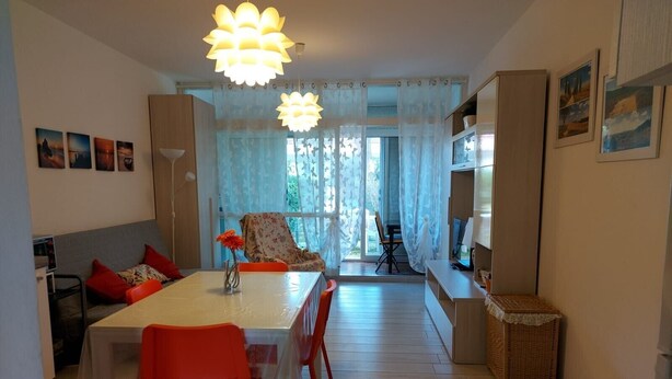 A dining area with a table, chairs, and a sofa. There is a television on a stand and a basket on the floor. - 'Prestige Apartment' with Shared Pool and Private Garden (Marina di Bibbona)