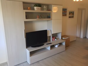 Un salon moderne avec un téléviseur à écran plat, une lampe et une étagère ornée d’objets décoratifs.
