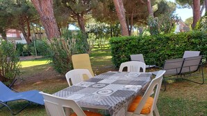 An outdoor dining area with a table covered in a patterned tablecloth, surrounded by white plastic chairs with orange cushions. - 'Prestige Apartment' with Shared Pool and Private Garden (Marina di Bibbona)