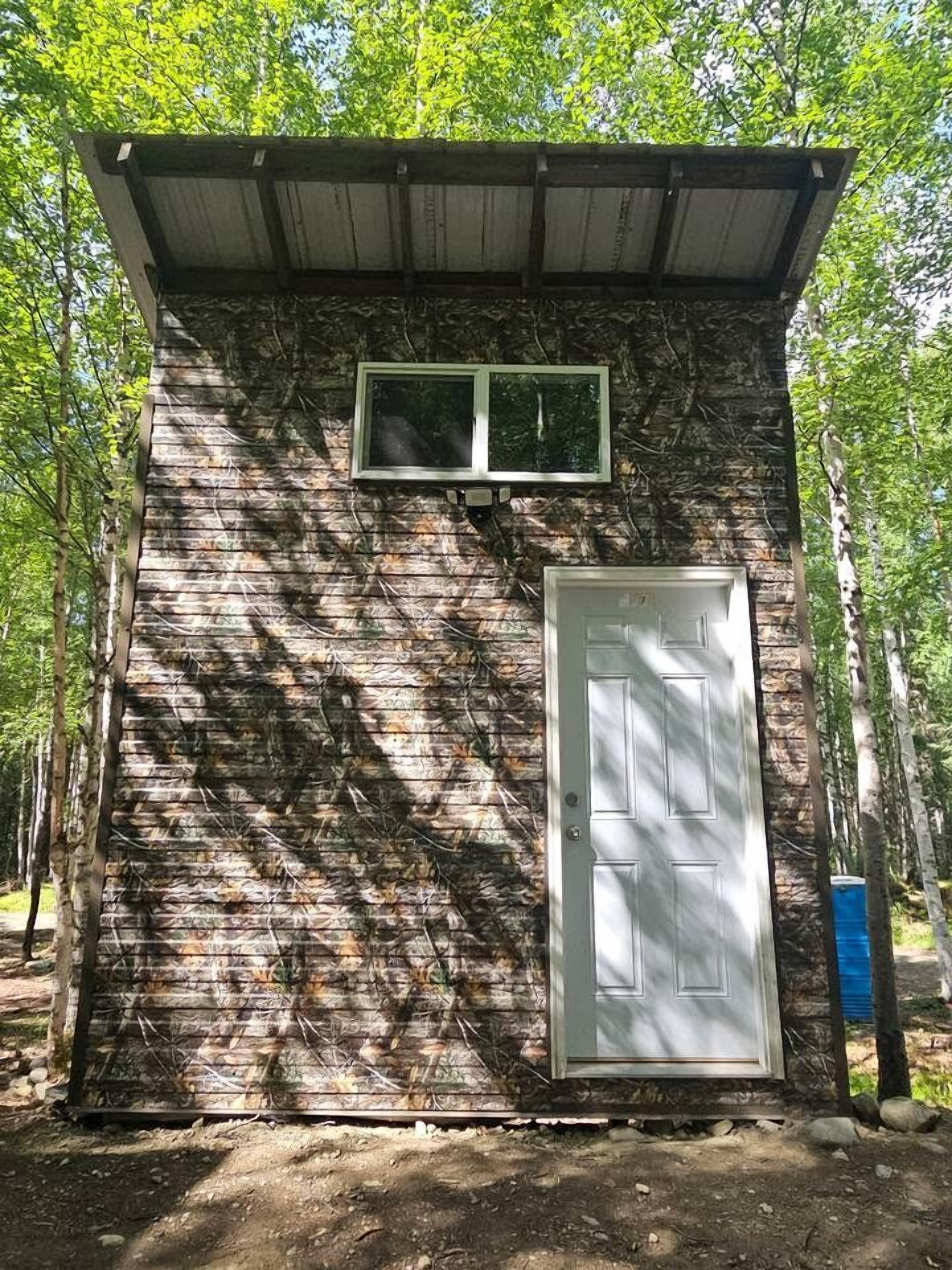 A small, single-room structure with a door and a window, surrounded by trees.