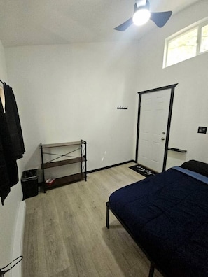 Een slaapkamer met een bed, een plank, een deur en een plafondventilator.