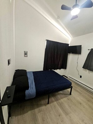 A bedroom with a bed, a ceiling fan, a TV, and a window with curtains. - Relaxing Mini Cabin Hideaway with Campground Amenities, Play Area & Firepit in Houston, Alaska (Houston)
