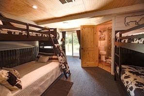 Une chambre avec des lits superposés, un plafond en bois, une porte donnant sur une salle de bain et une vue sur l’extérieur.