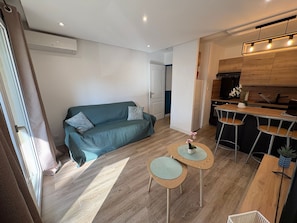 Ein modernes Wohnzimmer mit einer Couch, zwei kleinen runden Tischen, einer Küchenzeile mit Barhocker und einem Kühlschrank.