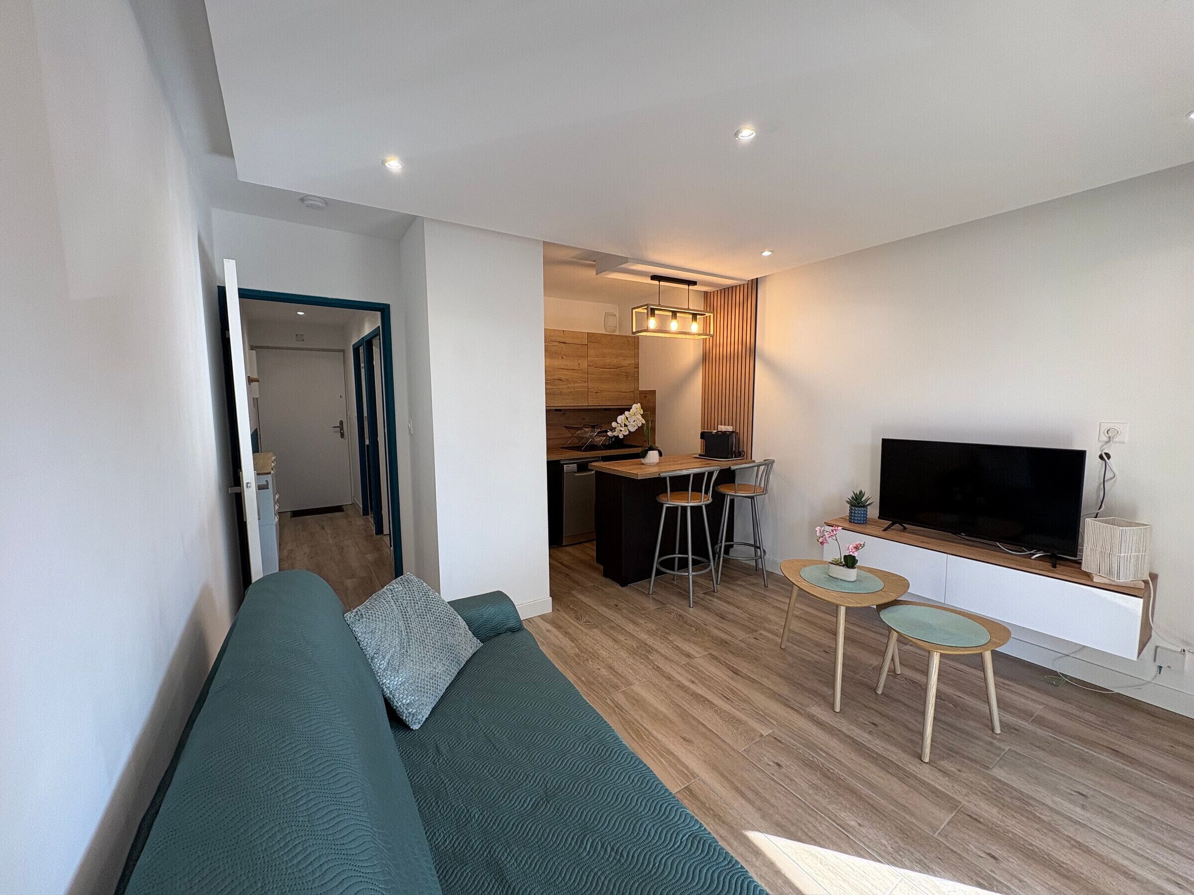 Un salon moderne avec un canapé, un téléviseur, un petit coin repas et une cuisine en arrière-plan.