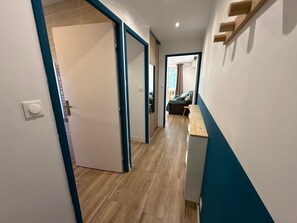 Ein Korridor mit Holzboden, einer Tür links und einer Bank rechts.
