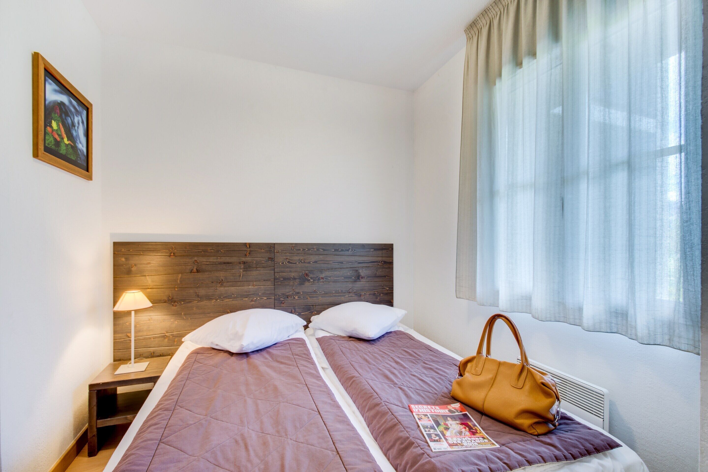 A neatly made bed with a wooden headboard, a bedside lamp, and a magazine on the bed.