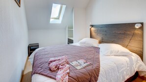 A bedroom with a wooden headboard, a skylight, a bed with a quilt, and a magazine on the bed. - Loudenvielle Stay With Alpine Views (Loudenvielle)