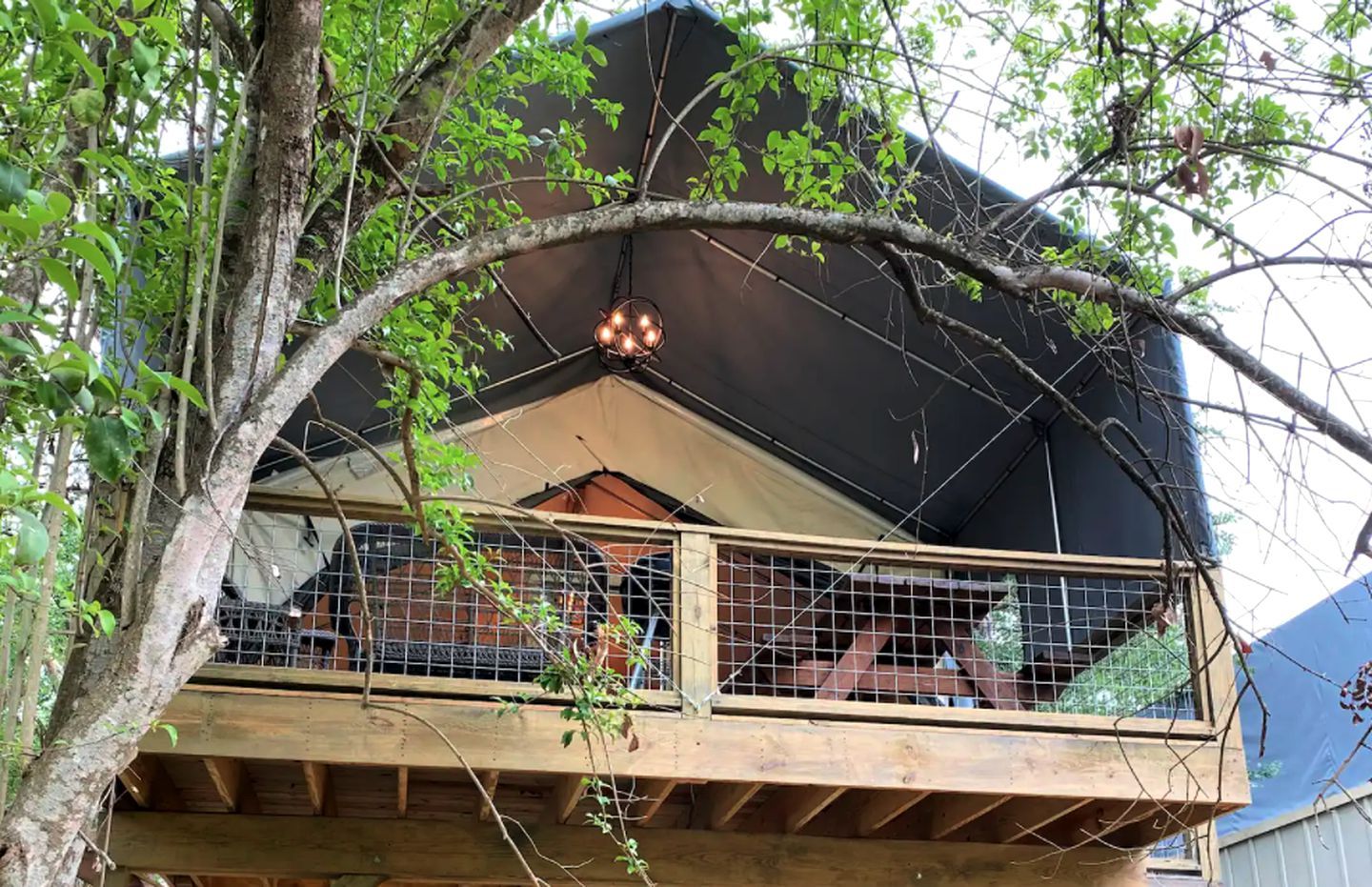 A wooden balcony with a metal railing, surrounded by trees and a building.