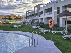 Un área de piscina con sillones de descanso y un flotador salvavidas, rodeada por un edificio moderno con balcones.