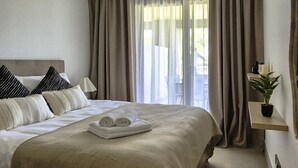 Een net opgemaakt bed met opgerolde handdoeken, een bedlampje en een kamerplant op een plank.