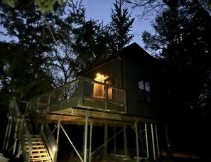 Une cabane dans les arbres dotée d’une terrasse en bois et d’un escalier menant à celle-ci.
