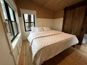 A bedroom with a large bed, wooden flooring, a window, and a door.