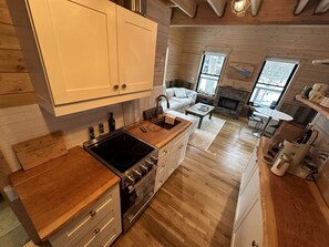 Una cocina con armarios de madera, estufa y lavamanos. Hay un comedor con mesa y sillas.
