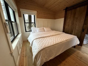 Un dormitorio con una cama grande, suelo de madera, una ventana y una puerta.