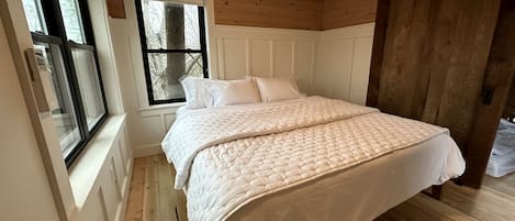 Un dormitorio con una cama grande, suelo de madera, una ventana y una puerta.