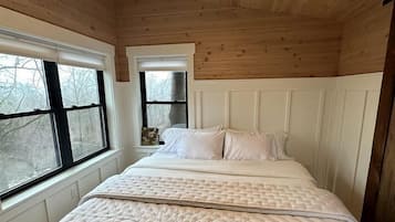 A bedroom with a wooden ceiling, a bed with white bedding, and two windows with blinds.