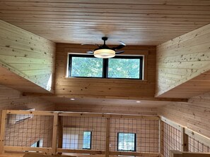 Un interior de madera con ventilador de techo, ventanas amplias y un muro con diseño de cuadrícula.