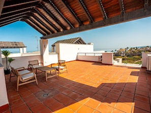 Una terraza en la azotea con vistas al mar, que incluye una pérgola, una mesa con sillas y una planta en maceta.