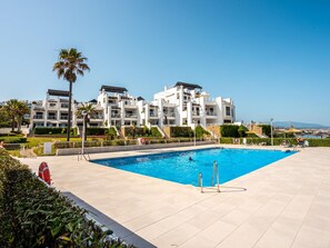 A swimming pool with a clear view of a modern building with multiple balconies and a landscaped garden. - Penthouse with sea view, 6 guests (Casares)